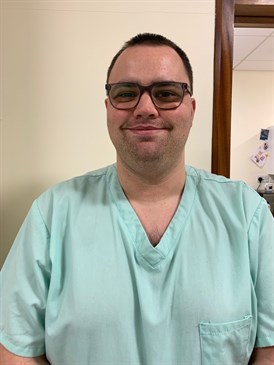 Aaron Carliell, a theatre support worker. Image is head and shoulders of him wearing scrubs