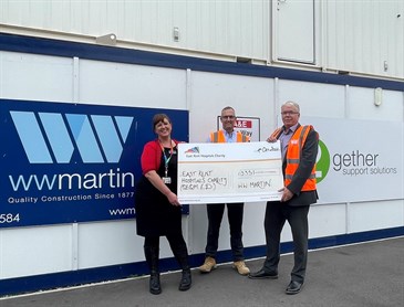 Dee Neligan receiving the cheque from Mike Darling, right, and Darren Offen from WW Martin. Image shows them holding a giant cheque in front of hordings with the WW Martin logo on