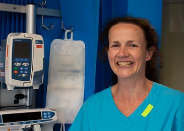 Ruth Tighe, a critical care consultant. She is wearing blue scrubs and pictured next to some medical equipment on the critical care unit