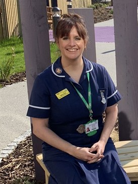 Abbi Smith, head and neck cancer clinical nurse specialist. Image shows Abbi sitting on a bench in a garden outside the Kent and Canterbury Hospital. She is wearing dark blue uniform