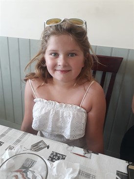 Abbie Paice, who has been helped by the play specialists over the years. She is sitting at a table in summer clothes and has sunglasses on top of her head.