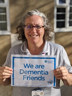 Ann McGovern, a dementia associate practitioner who will take part in the virtual London marathon. She is pictured in uniform holding a 'we are dementia friends' sign and smiling at the camera