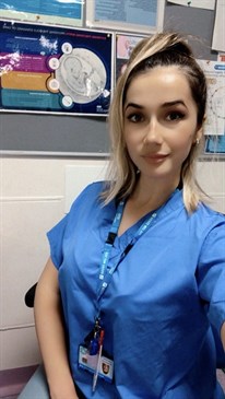 Arjola Koci, maternity support worker. She is wearing blue scrubs and looking at the camera.