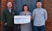 Avatar of Matt Champ, Dee Neligan and Callum Tydeman. Image shows them standing together holding a cheque. They are outside in front of a blue door
