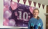 Avatar of Molly Sayer on her birthday. Image shows a 10 year old girl standing in front of a banner that says happy 10th birthday on it