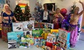 Avatar of belly dancers from Sparkles Belly Dance classes with gifts they donated. Image shows three belly dancers in costume and one member of staff, not in clinical uniform, with a Christmas tree and toys. They are doing a belly dance pose with the