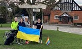 Avatar of the four friends who are undertaking a charity challenge for Ukraine. Image shows four women standing by a village sign holding a Ukrainian flag