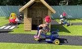 Avatar of youngsters learning about road safety in their new garden. Image shows a child on a trike riding on a road marked out in a garden. There is a zebra crossing and road signs, and a shed in the background.