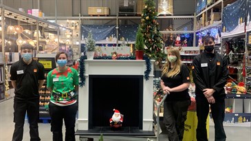 B&Q staff with the fireplaces. Four people are pictured in the store, two on each side of the fireplace. There is a small Santa figure in the middle of the fireplace and a Christmas tree in the background