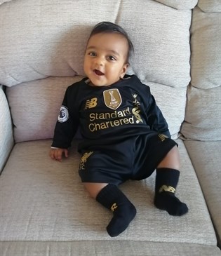Baby Liyah Sharma, whose dad is planning a 24-hour podcast to raise money for East Kent Hospitals Charity's Tiny Toes Appeal. Liyah is wearing a football outfit and sitting on a cream armchair.