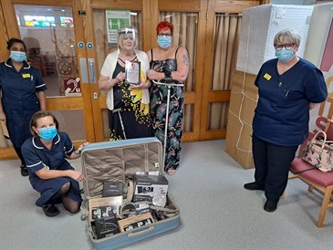 Bob Tomkins' wife Anne and daughter Corena with Kings D staff and the items they have donated. They are pictured inside the hospital, Anne and Corena are standing together. There are three members of staff in the photo, one is kneeling by a suitcase 