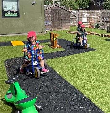Children enjoying the new garden at Little Oaks Ashford. Image shows children on trikes riding on a road layout in their new garden