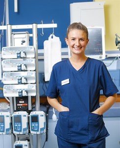 A nurse in the ITU with some equipment visible behind her. She is wearing blue scrubs