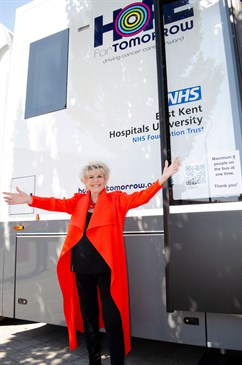 Gloria Hunniford with the new Caron mobile cancer care unit. Image shows Gloria, with her arms outstretched, standing in front of the new unit