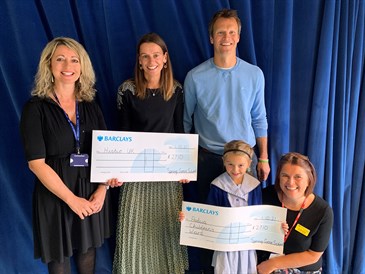 Daisy Loudon cheque presentation. Image shows Daisy, five, holding a cheque with Dr Jill Urand, who is kneeling next to her. Her parents are standing behind her holding another cheque and the head teacher of the school is standing on the left. There 
