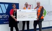 Avatar of Dee Neligan receiving the cheque from Mike Darling, right, and Darren Offen from WW Martin. Image shows them holding a giant cheque in front of hordings with the WW Martin logo on