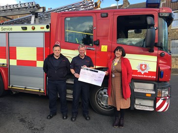 Avatar of Dee Neligan receiving the cheque from Kent Fire and Rescue Service. Image shows Dee standing with two firefighters in front of a fire engine. They are holding a cheque.