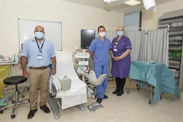 From left, Sashi Kommu, Curtis Phelan, and Jenny Hansen. They are pictured in a clinical room with a medical chair with stirrups. They are all wearing face masks.