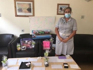 Gemma McNutt with the raffle prizes. Photo shows Gemma in uniform and a mask  in a room with chairs and a coffee table. Prizes and vouchers are laid out on the table and chairs.