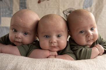 George, Harry and Oscar, triplets who appeared in Call The Midwife. Image shows three babies, aged around eight months old. They are all looking at the camera, with their heads close together, propped up on a blanket.