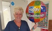 Avatar of Gill Miller on her last day. Image shows her holding a balloon that says Happy Retirement. 