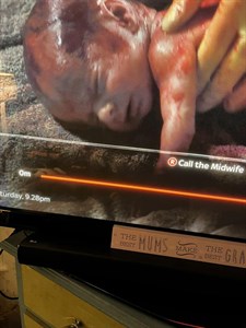 Screenshot of Harry appearing in Call The Midwife. Image shows a TV screen with a baby looking like it is newly delivered, with gloved hands holding it