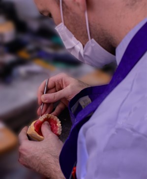 James Abbott in the maxillofacial prosthetics lab. Photo is taken from behind and shows him painting a dental prosthesis