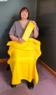Jayne Flood demonstrates the yellow falls kit. Photo shows Jayne sitting in a chair holding yellow socks with a yellow blaknket on her lap.