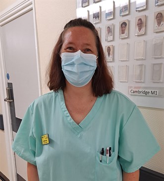 Judith Sloan, a former teacher who has returned to nursing at East Kent Hospitals. She is pictured wearing scrubs and a mask in a corridor on the ward.