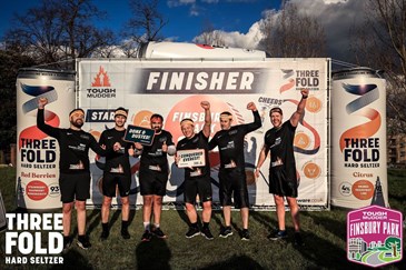 Kent Construction Consultants after their charity challenge. Image shows a group of six men wearing black shorts and t-shirts standing in front of a sign that says finishers. One is holding a certificate