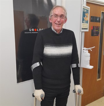 Malcolm Cole, who had robotic surgery to remove his prostate. He is pictured standing in a hospital corridor in front of a sign for the urology department. He is using crutches.