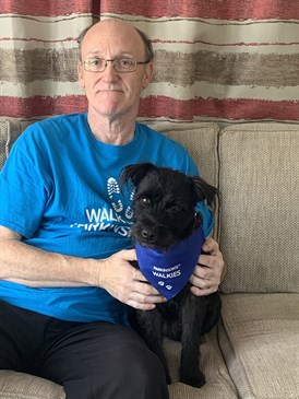 Avatar of Mark Bailey, an HCA with Parkinson's. He is sitting on a sofa with a small black dog looking at the camera, wearing a Parkinson's UK t-shirt. The dog also has a Parkinson's UK bandana
