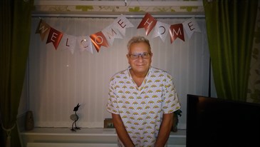 Mark Wignall when he returned home from hospital. He is wearing a t-shirt with rainbows on and is pictured inside, standing under welcome home bunting