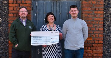 Matt Champ, Dee Neligan and Callum Tydeman. Image shows them standing together holding a cheque. They are outside in front of a blue door