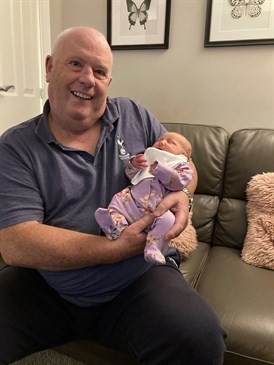 Michelle Keen's dad David Hayman with baby Isabelle. He is sitting on a sofa holding her.