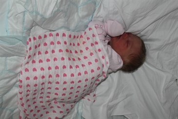 Molly when she was born. Image shows baby on a bed wearing a pink babygrow and covered with a blanket with pink hearts
