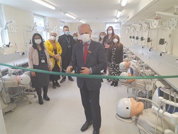 Opening of the new dental lab at KCH by Peter Briggs from HEE. Image shows Peter cutting a ribbon with people behind looking on. The lab has stations set up to look like dentists' chairs with model heads for students to work on.