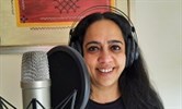 Avatar of Rema Iyer, a consultant at the QEQM who has recorded a song about a humble rice dish. She is pictured by a professional-looking microphone and is wearing headphones.