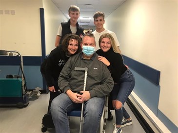 Avatar of Richard Claxton being reunited with his family after being treated for Covid 19. They are pictured in a hospital corridor - Richard is in the middle in a wheelchair wearing a mask and holding crutches, his family are around him all looking 
