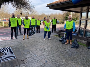 Ashford Rotary Club litter pickers. The photos shows people wearing high-vis vests standing outside the William Harvey Hospital with the car park in the background. People at the front are holding litter pickers and black bags.