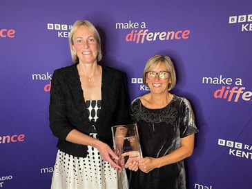 Sarah Gotke and Lucy Mummery with their award. Image shows them in front of a Make a Difference backdrop, holding a glass award