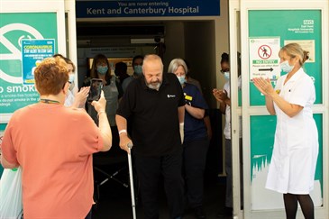 Jim Beverton leaving hospital after 147 days. The photo shows Jim walking out of the hospital doors, using just a stick, watched by staff who are applauding.