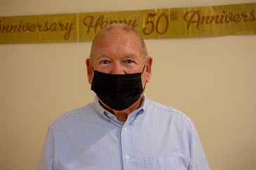 Michael Phillips, who had a kidney transplant 50 years ago. He is pictured in front of a banner saying 'happy 50th anniversary' and is wearing a mask