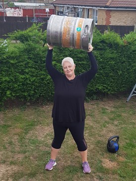 Nikki Burrows in her garden holding a barrel over her head as part of her training for her charity challenge raising money for CRY in memory of her son Rhys