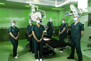 Staff inside one of the operating theatres at the Elective Orthopaedic Centre. The lighting is green and the staff are wearing scrubs and standing around an operating table with lights and machines in the background