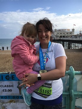 Susanna Thomas, holding daughter Amy, in front of Brighton Pier. Susanna is in running gear and wearing a medal