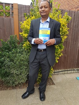 Full length photo of Thadeus Matemba outside holding the book he has written about prostate cancer