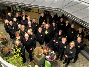 Thanet Rock Choir outside the Viking Day Unit at QEQM. Photo is taken from above and shows a group of people in rock choir uniform outside the unit in a garden area.