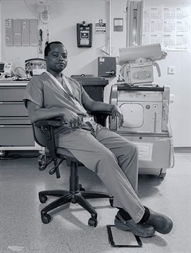 Kyle Tallett's chosen image of colleague Allen Matembo after a 12-hour nightshift. Black and white photo of Allen in scrubs sitting in a chair in a room with radiography equipment