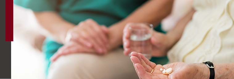 Nurse holding older patients hand as they hold pills and a glass of water